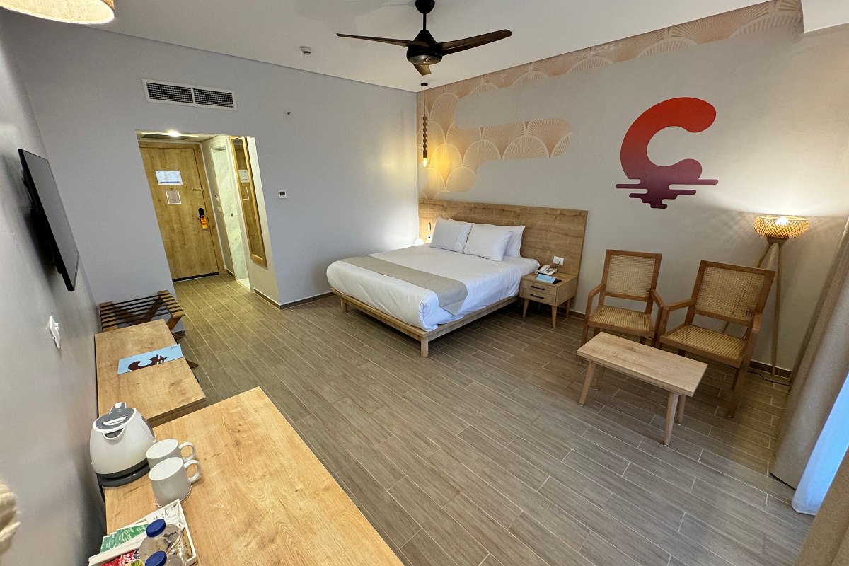 Helles Hotelzimmer mit Doppelbett, Holzboden, Nachttischen und einem kleinen Tisch mit Obstkorb.