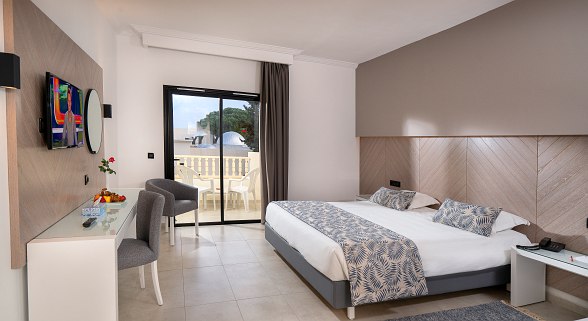 Modernes Hotelzimmer mit Doppelbett, Schreibtisch, Balkon und hellem, neutralem Design.