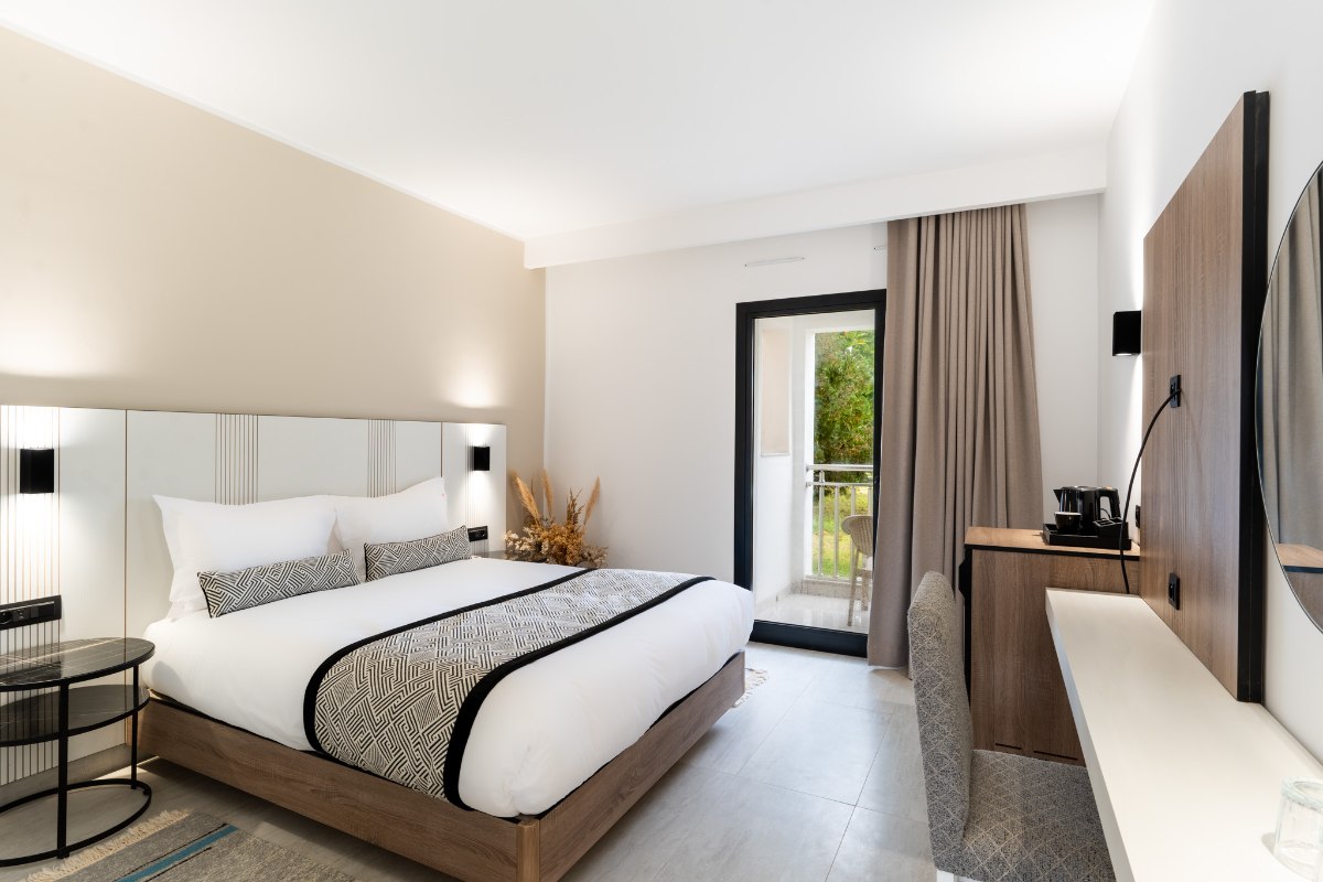 Modernes Hotelzimmer mit Doppelbett, blauer Akzentwand, farbenfroher Wandkunst und Balkon mit Gartenblick.