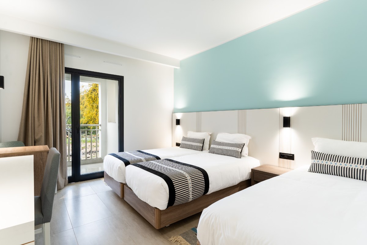 Modernes Hotelzimmer mit Holzdach und dezenten Beleuchtungselementen, ausgestattet mit großem Bett, braunem Sofa, Couchtisch und Wandfernseher.