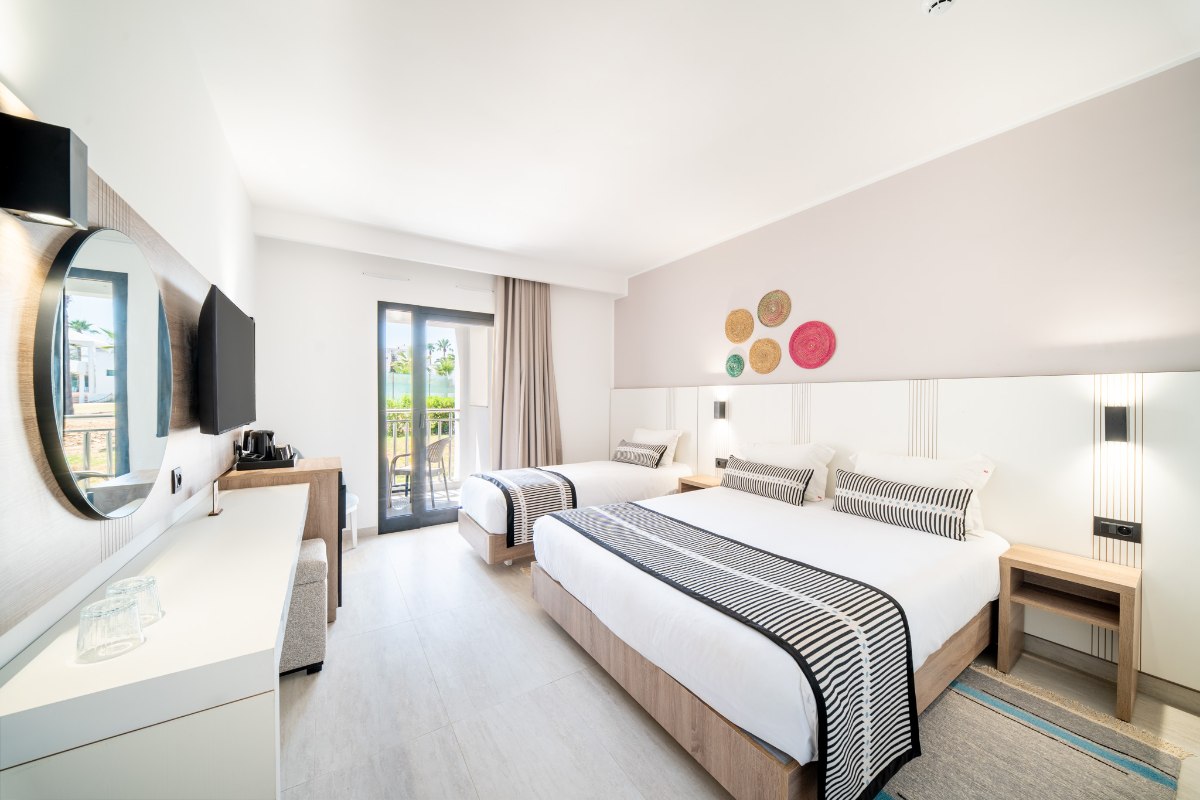 Modernes Hotelzimmer mit Holzdach und dezenten Beleuchtungselementen, ausgestattet mit großem Bett, braunem Sofa, Couchtisch und Wandfernseher.