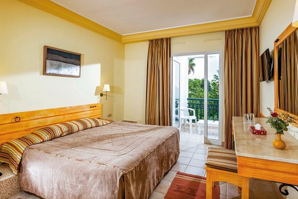 Modernes Hotelzimmer mit Holzdach und dezenten Beleuchtungselementen, ausgestattet mit großem Bett, braunem Sofa, Couchtisch und Wandfernseher.