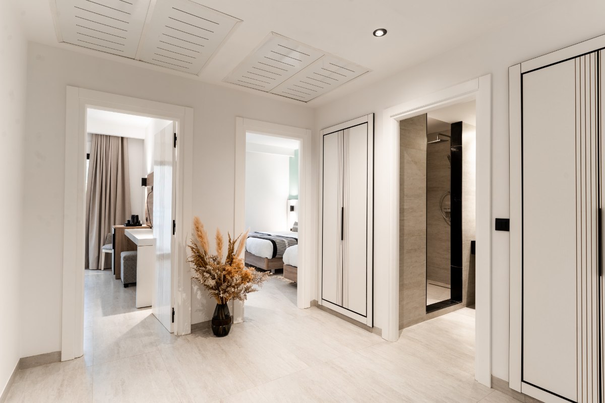 Helles Hotelzimmer mit zwei Einzelbetten, rotem Sofa, großem Blumenbild und Balkon mit Meerblick.