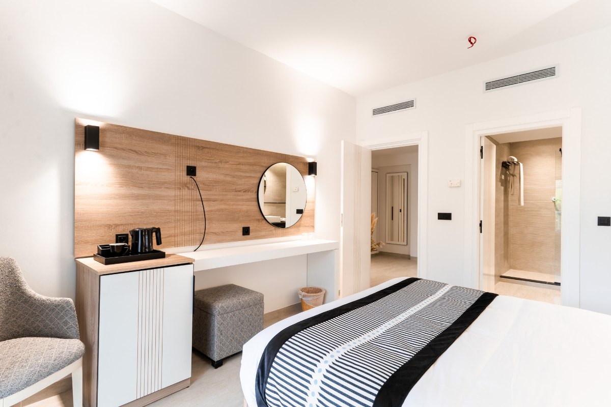 Modernes Hotelzimmer mit großem Bett, blauer Wandgestaltung, Balkon und Blick auf Palmen.