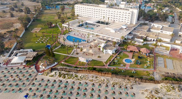 Luftaufnahme eines großen Hotels mit Pool, Spielplatz, Liegestühlen am Strand und weitläufigem Garten.
