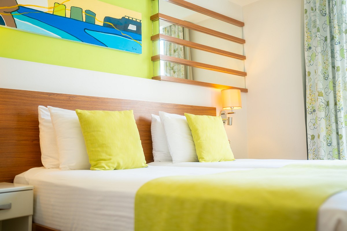 Helles Hotelzimmer mit zwei Einzelbetten, grüner Deko, Balkonzugang und modernem Design.