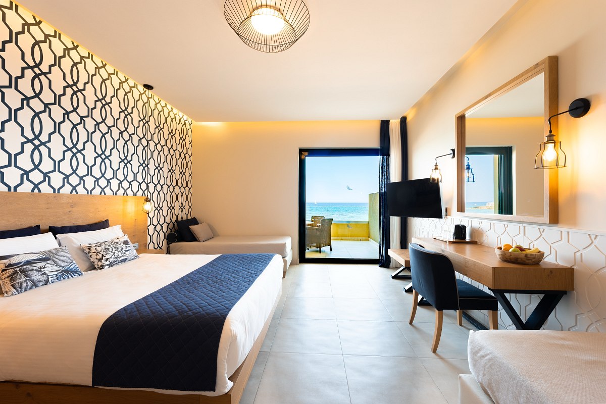 Modernes Hotelzimmer mit Doppelbett, Sofa, Schreibtisch, Meerblick und Balkon mit Sitzgelegenheit.