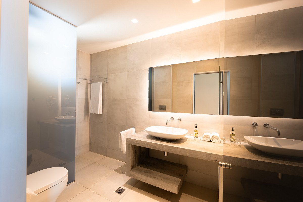 Modernes Badezimmer mit Doppelwaschbecken, großem Spiegel, Glasdusche, Toilette und hellen Fliesen.