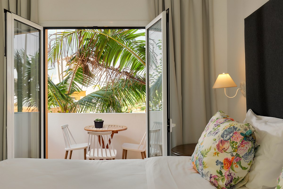 Modernes Hotelzimmer mit Doppelbett, Sofa, Schreibtisch, Meerblick und Balkon mit Sitzgelegenheit.