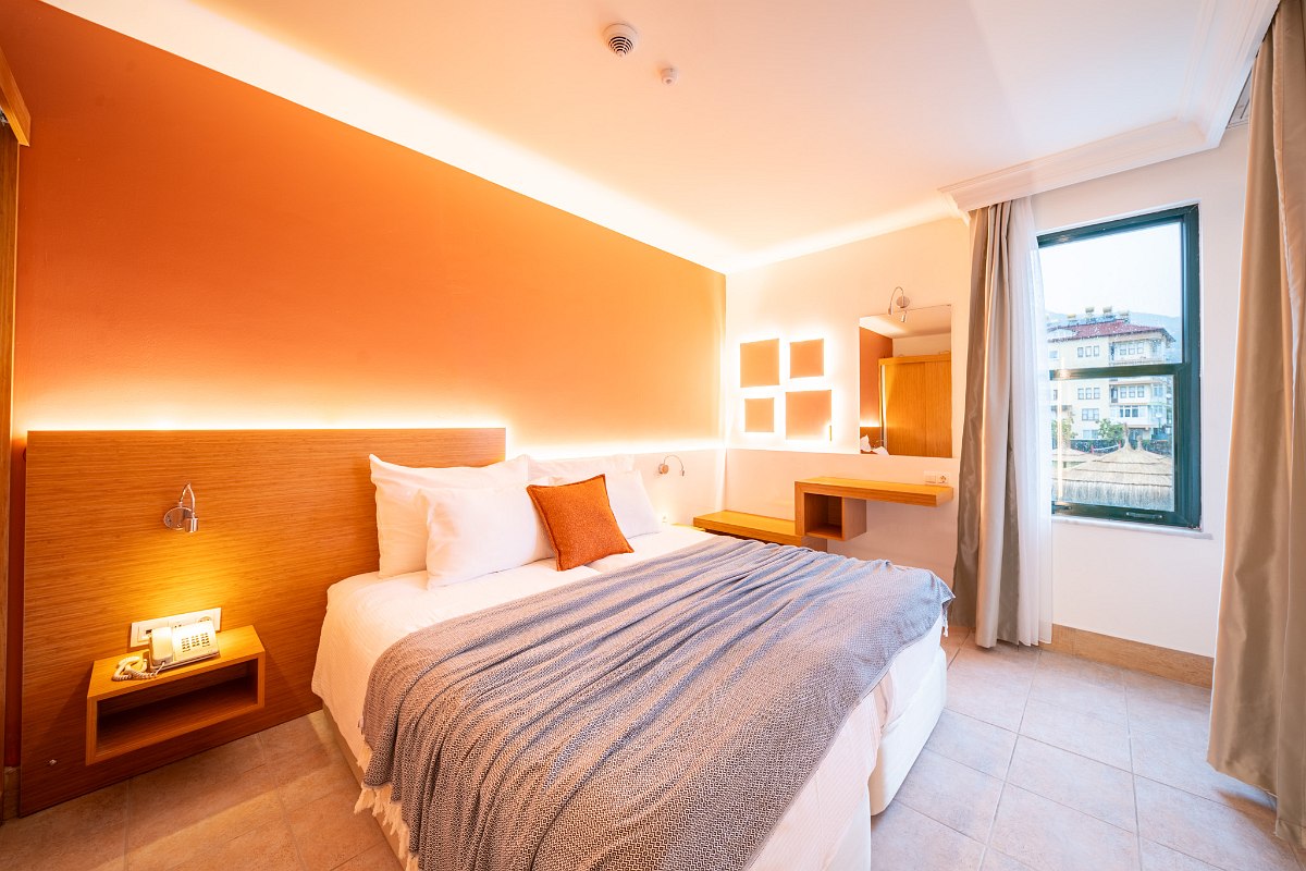 Helles Hotelzimmer mit zwei Einzelbetten, bunter Deko, Balkonzugang und Fliesenboden.