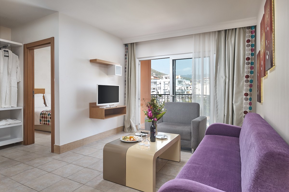 Hell eingerichtetes Zimmer mit zwei Einzelbetten, violettem Sofa, Poolblick, Wohnbereich und Schlafbereich, zwei Klimaanlagen, Nichtraucher Zimmer, Fliesenboden.