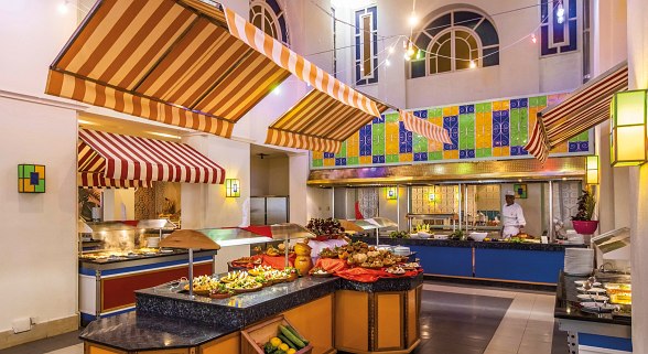 Bunt dekoriertes Buffetrestaurant mit Markthallen-Flair, reich gedeckten Speisenstationen und Kochbereich.