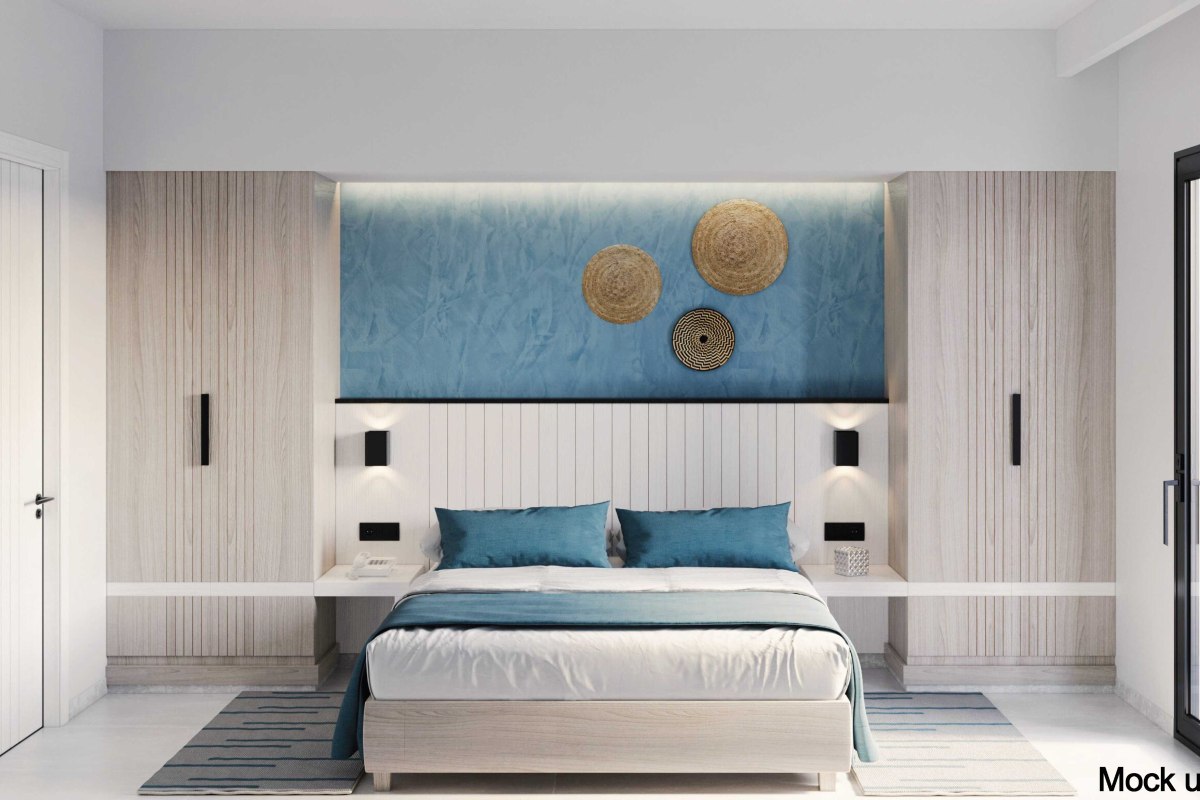 A bright hotel room with a large bed, blue and beige accents, patterned rugs, a balcony with outdoor seating, and a decorative blue wall.