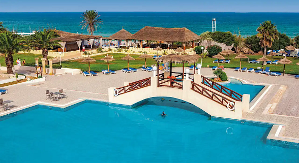 A colorful water slide complex with multiple slides of different shapes and colors, reflected in a calm blue pool, surrounded by palm trees.