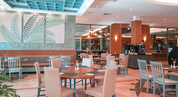 Modern restaurant with wooden tables, white and gray chairs, decorative plants, and large windows
