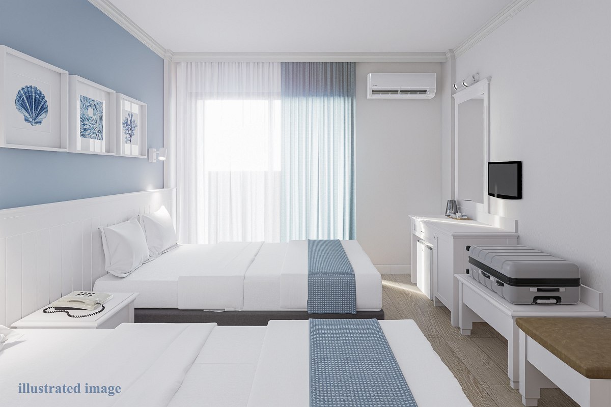 Bright and simple hotel room with two twin beds, white bedding with light blue runners. The room features a small TV mounted on the wall, a white vanity desk with a mirror, and a luggage rack with a suitcase. Large window with sheer curtains and an air conditioner above it.