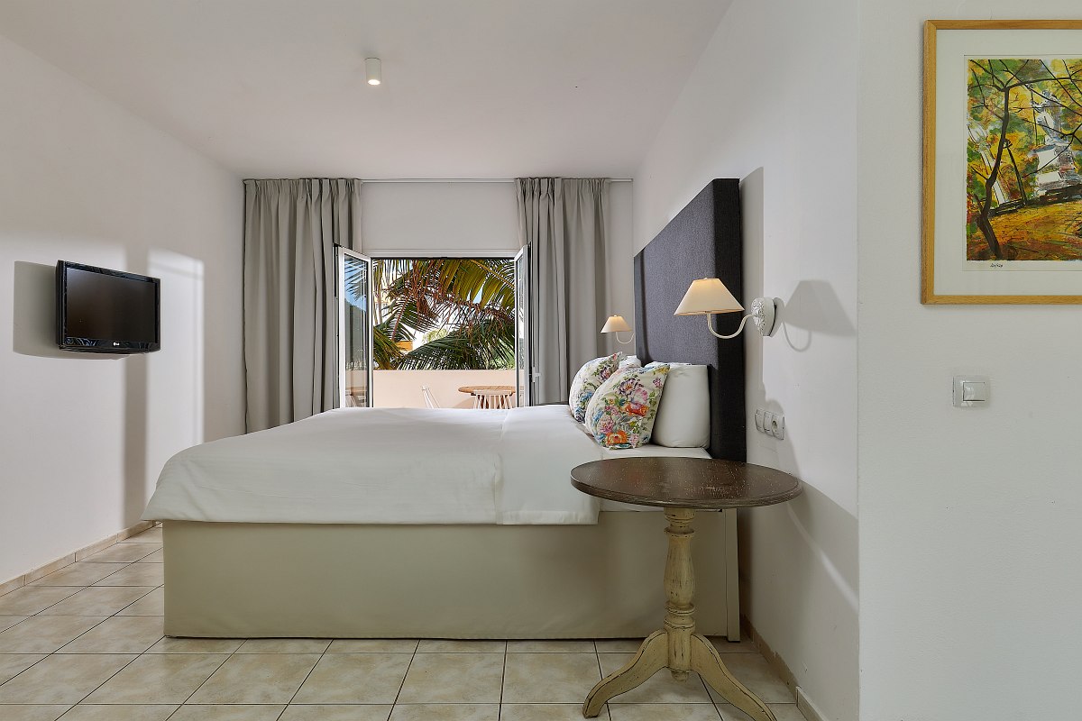 Modern hotel room with double bed, sofa, desk, sea view and balcony with seating.