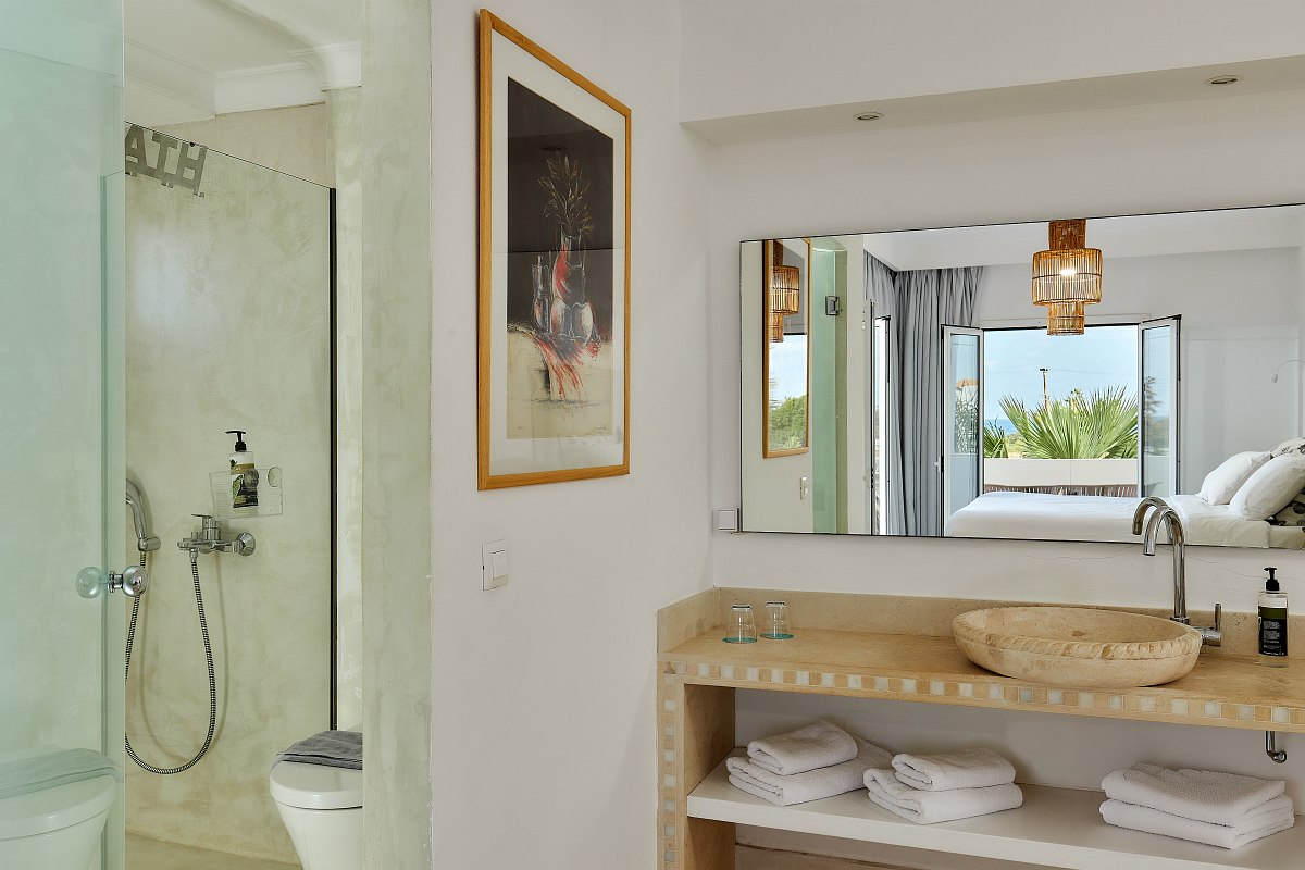 Bright hotel room with double bed, patterned walls, sofa, desk, wooden wardrobe and turquoise door.