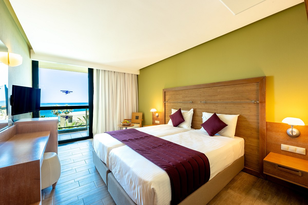 Modern hotel room with double bed, green-painted wall, balcony with sea view and cozy seating area.