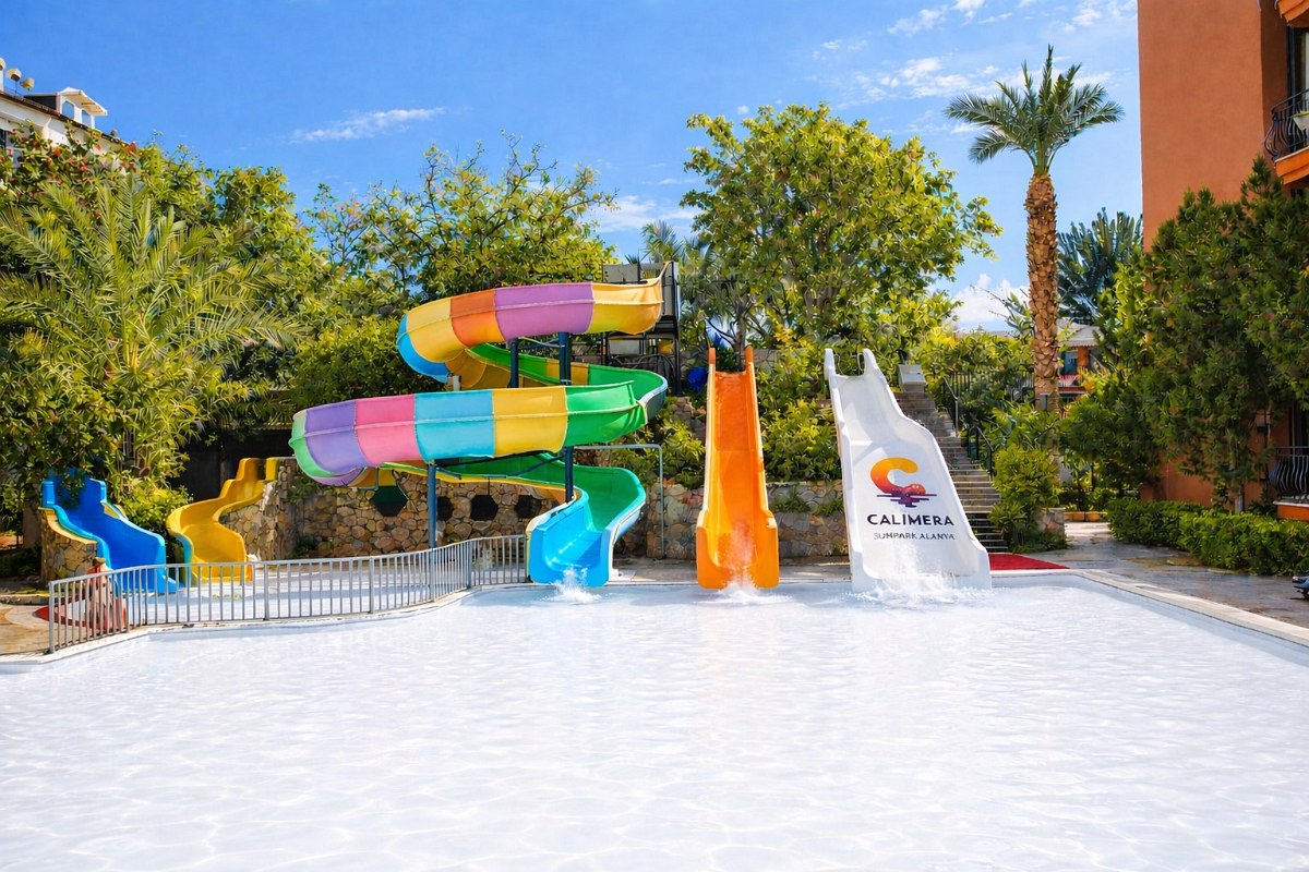 Pool with colourful water slides and blue deckchairs at the edge of the pool, next to a modern, bright hotel building.